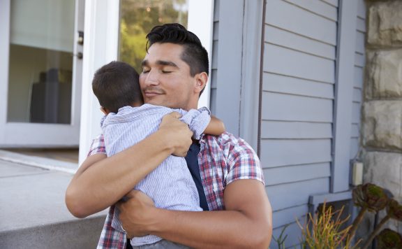 Father Hugging Son Sitting On Steps Outside Home